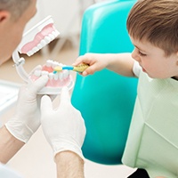 Dentist showing young boy how to brush teeth