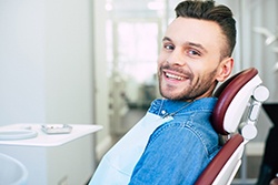 Man in denim shirt smiling while sitting in dentist's chair