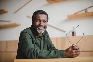 older man sitting at table and holding his glasses 