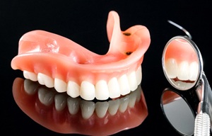 An upper implant denture sitting next to dental instruments in San Antonio