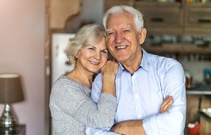 An older couple hugging and smiling in their home after completing dental implant treatment in San Antonio