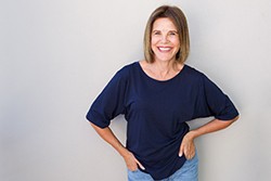 Woman in blue shirt and jeans smiling with hands on hips