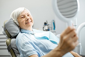 An older woman looks in the mirror and smiles after using her dental insurance in San Antonio to pay for necessary treatment