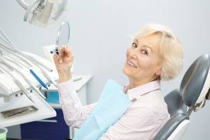 Senior female dental patient holding mirror and smiling
